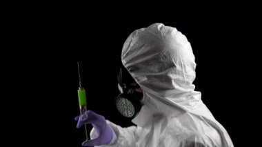 Kimyasal koruma giysisi içinde bir laboratuvar çalışanı elinde siyah bir arka plan üzerinde yeşil enjeksiyonlu bir şırınga tutuyor.