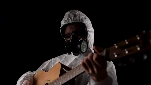 呼吸器と眼鏡の化学保護スーツの男が黒い背景にギターを演じる — ストック動画