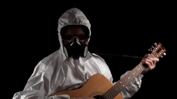 身着化学防护服 头戴呼吸器 戴着眼镜的男子在黑色背景下弹奏吉他 — 图库视频影像