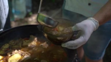 Aşçı büyük bir dökme demir kazana bir kepçe et çorbası döker. Yavaş çekim