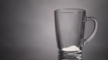 Kaşık şekeri gri arka plandaki cam bardağa dökülür. Yavaş çekim