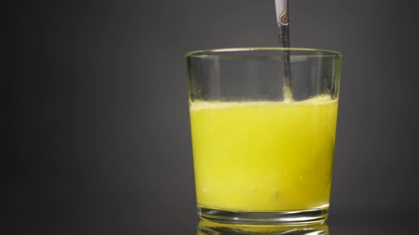 在灰色的背景上用勺子在玻璃杯烧杯中搅拌黄色混合物 慢动作 — 图库视频影像