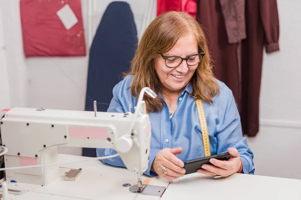 Chilean adult senior portrait. self-employment dressmaker at workplace with textile equipment like sewing machine.