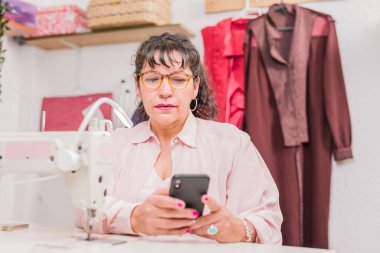 Latin Amerikalı olgun kadın moda endüstrisi atölyesinde. Dikiş makinesi ve giysi gibi el işi ve tekstil malzemeleri. örgü tasarımcısı.