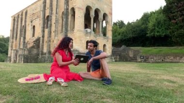 Oviedo 'daki Santa Maria del Naranco Roma öncesi kilise, UNESCO ortaçağ. Latin kadın ve Hintli adam bir tablette tatil bilgileri arıyorlar.