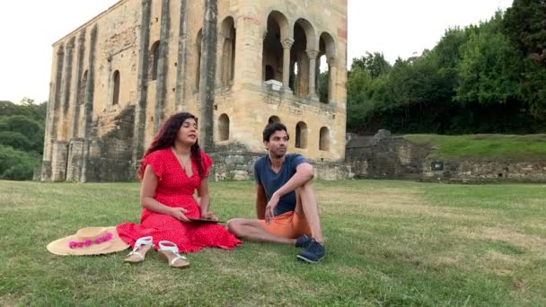 ユネスコの中世のオビエドにあるサンタ マリア ナランコ教会 ラテン系の女性とインド人男性がタブレットで休暇情報を探しています — ストック動画