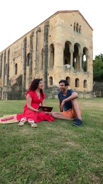 ユネスコの中世のオビエドにあるサンタ マリア ナランコ教会 ラテン系の女性とインド人男性がタブレットで休暇情報を探しています — ストック動画