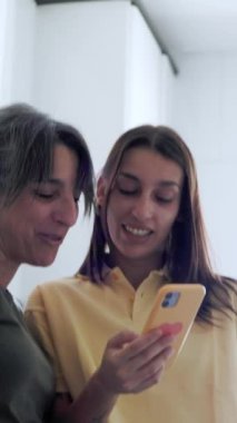 Anne ve kızı birlikte güzel vakit geçirmenin keyfini çıkarıyorlar, akıllı telefondan gülüyorlar.