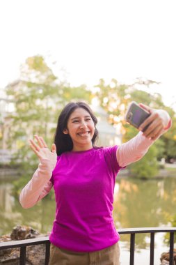 El Etiro Park, Madrid, İspanya 'daki akıllı telefonuyla yaptığı bir video görüşmesi sırasında gülümseyen genç bir kadın. Madrid, Parque El Retiro Palacio de Cristal 'in önü