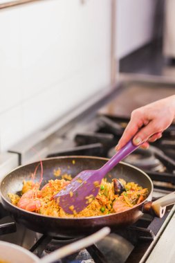 Aşçı spatula kullanarak fırının tepsisinde renkli deniz ürünleri pilavı pişiriyor. Madrid 'de bir restoranın mutfağında geleneksel ekvador yemeği hazırlıyor.