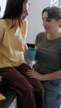 Anne ve kızı, mutfaklarında, kahkahalarını ve sohbetlerini kahve eşliğinde paylaşarak keyifli bir an geçiriyorlar.