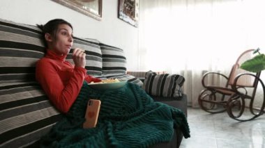Genç bir kadın kanepede keyfine bakıyor televizyon izlerken atıştırıyor ya da dizüstü bilgisayarında film seyrediyor. Kapalı mekan sahnesi
