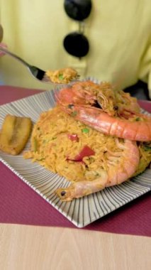 Lezzetli bir tabak arroz marinero 'nun tadını çıkaran bir kadın canlı bir restoranda karides pilavı yiyor. 