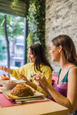 Two women savor traditional ecuadorian dishes in a madrid restaurant, indulging in the vibrant flavors of south american cuisine clipart