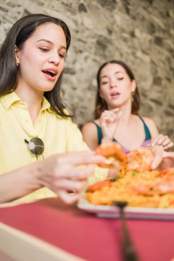 Two women are savoring a flavorful ecuadorian seafood dish with prawns and rice in a madrid restaurant, engaging in lively conversation clipart