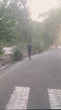Genç Latin bir kadın sisli bir sabah boyunca park yolunda düzenli bir şekilde koşmaya devam ediyor. Vücut geliştirme ve sağlıklı yaşam tarzını somutlaştırıyor.