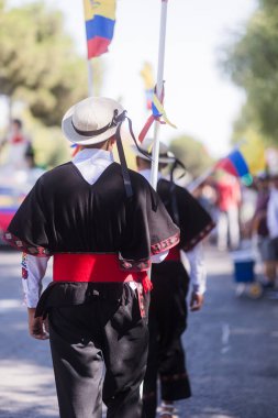 Men wearing traditional costumes are walking in a parade, celebrating their hispanic heritage with colorful flags and festive attire clipart