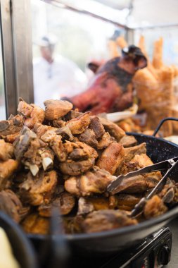 Metal tongs grabbing pieces of fried pork meat, served in a large black bowl during a hispanicity day parade clipart