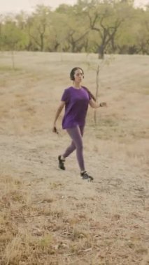Spor kıyafetleri ve kulaklık takan Latin yetişkin bir kadın müzik dinlerken tarlada yürüyor.