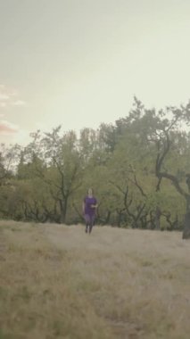 Kendini adamış kadın sporcu, enerjik sabah antrenmanı sırasında ağaçlarla çevrili, güneşli alanda koşuyor.