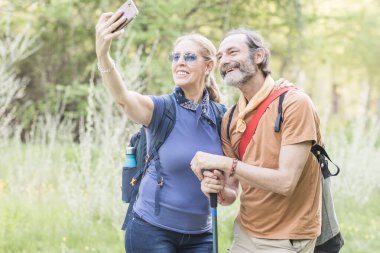 Madrid, İspanya 'da doğa yürüyüşünün tadını çıkarırken akıllı telefonuyla selfie çeken mutlu yürüyüşçü çift.