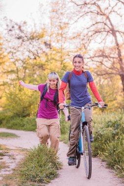 İki neşeli bayan yürüyüşçü, biri bisiklet sürüyor, güneşi emiyor ve kırsal alanda güzel bir günün tadını çıkarıyor.