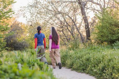İki kadın, yemyeşil ve ağaçlarla çevrili doğa yolunda huzurlu bir yürüyüş yapıyorlar.