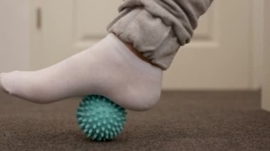 Düz taban düzeltme yapan bir kadın masaj topu kullanarak jimnastik yapıyor. Ayak kaslarında miyofasyal gevşeme. Hallux valgus. Acıyor. Düz taban tanımlaması. Evde kişisel bakım uygulamaları, sağlık hizmetleri