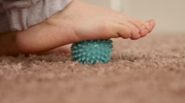 Düz taban düzeltme yapan bir kadın masaj topu kullanarak jimnastik yapıyor. Ayak kaslarında miyofasyal gevşeme. Hallux valgus. Acıyor. Düz taban tanımlaması. Evde kişisel bakım uygulamaları, sağlık hizmetleri