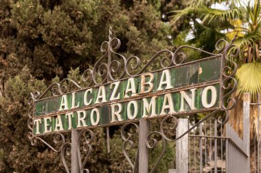 Malaga, İspanya - 26-01-2024: AlCAZABA TEATRO ROMANO adlı klasik metal simgesi gür ağaçlar arasında. Roma Tiyatrosu, Malaga 'nın en eski anıtıdır.