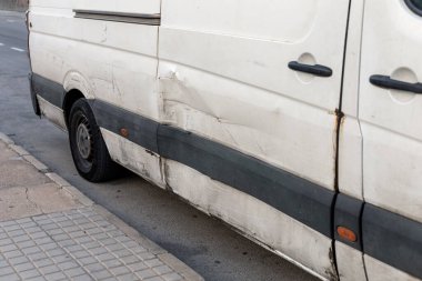 Yan tarafında gözle görülür hasar olan, çizikler ve çizikler olan beyaz bir arabanın detaylı görüntüsü. Araç tamiri, sigorta vaka çalışmaları ve şehir içi sürüş risklerini göstermek için mükemmel.