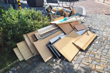 Bir kaldırım taşı caddesinde yığılmış bir yığın ev eşyası ve mobilya, kentsel bir çevrede toplu atık toplama gününü resmediyor.