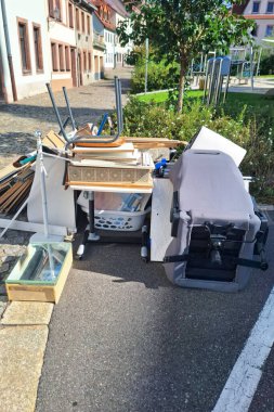Altüst olmuş ofis sandalyesi, ahşap tahtalar, kaldırımı karıştıran ev mobilyaları, kentsel atık yönetimi sorunlarını yansıtan, sorumluluk gereksinimini yansıtan eşyalar. Dikey resim