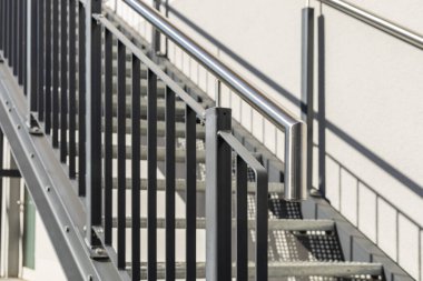 Metal parmaklıklar çelik merdiveni destekliyor, çağdaş bir mimari tarzı sergiliyor. Parlak ışık, öğlene doğru temiz ve minimalist bir çevreyi yansıtan materyalleri vurguluyor.