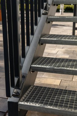 Dayanıklı metal merdivenler, güneşli açık hava bahçesindeki yükseltilmiş platforma erişim sağlar. Basamaklarda güvenlik için ızgara desenli fonksiyonel bir tasarım var. Metal yapı, kaynak, çelik merdiven.