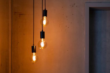 Tavandan asılı duran üç dekoratif ampul, desenli bir duvara sıcak bir parıltı saçıyor. Işıklar odanın rahat ve modern atmosferini arttırıyor..