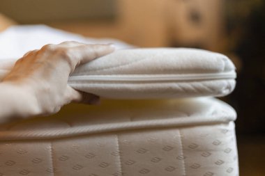 Bir el, hafifçe aydınlatılmış yatak odasındaki bir yataktan rahatlama tabakasını nazikçe kaldırır. Yatak temiz ve davetkar görünüyor, dinlenmeye ve dinlenmeye hazır..