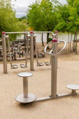 Kamu çalışma istasyonunda, yeşil alanlarla çevrili sakin bir gölün yanındaki parkta bulunan metalik fitness makineleri açık hava egzersizleri için idealdir..