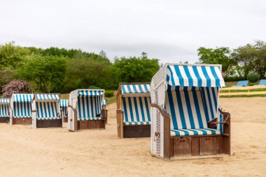 Kumlu zemine yerleştirilmiş canlı çizgili plaj sandalyeleri rahatlamak ve bulutlu gökyüzünün altında dinlenmek için barışçıl bir geri çekilme yaratır..