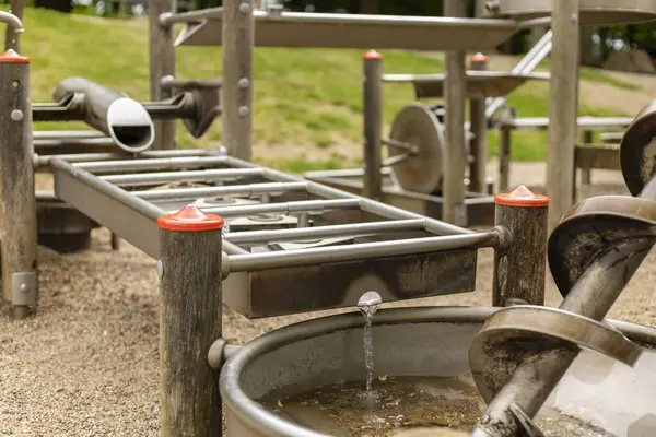 Çocuklar, su kanalları ve dönen spiral borular gibi etkileşimli elementlerin yer aldığı ve yaz eğlencesi için mükemmel olan bir su oyun alanının keyfini çıkarıyorlar. Aileler neşeli atmosferin tadını çıkarmak için toplanırlar..