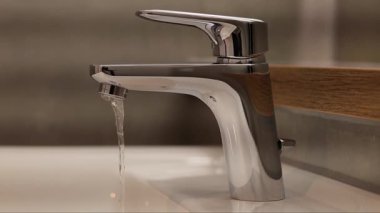 Modern krom musluk zarif bir şekilde el değmemiş bir banyo lavabosuna su döküyor. Şık tasarım, minimalist dekoru tamamlıyor. Huzurlu atmosferi geliştiriyor..