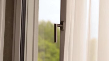 Açık bir pencere, güneş ışığı içeri süzülürken odanın içinde serinletici bir esintinin akmasına izin verir ve perdelerin usulca dans etmesine neden olur. Dışarıdaki doğa canlı ve canlı. Atmosferi güçlendiriyor..