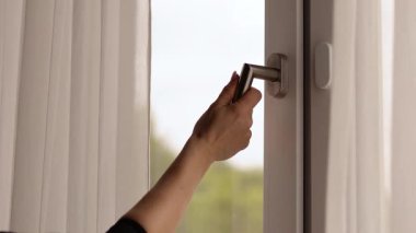 Birisi pencerenin koluna uzanarak onu açar ve sıcak odaya temiz hava almaya davet eder. Doğal güneş ışığı uzayı aydınlatır ve sakin bir atmosfer yaratır..