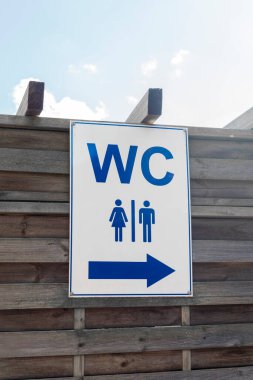 Açık tuvalet tabelasında erkek ve kadın tuvaletleri için semboller var. Tabela solda, tahta bir yapıya monte edilmiş, tipik açık hava ayarları..