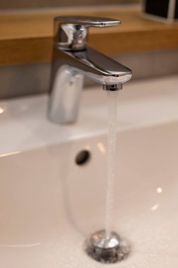 Pürüzsüz bir krom musluk, el değmemiş beyaz bir lavaboya, minimalist estetik ve temiz çizgilerle modern banyo tasarımı sergiliyor..