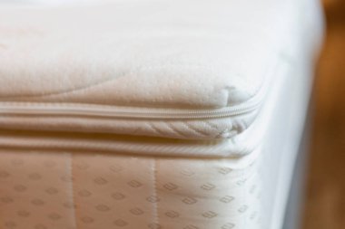 Yakın plan, yumuşak kumaşı ve iyi ışıklandırılmış bir çevredeki ayrıntılı dikişleri vurgulayan görünür bir fermuarla bir yatağın kenarını yakalıyor..
