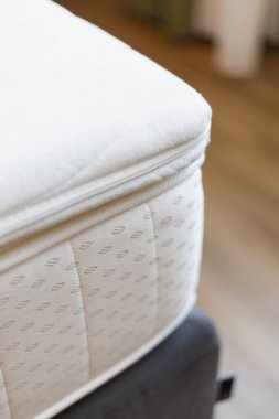 Modern bir yatak odasındaki şiltenin üzerinde yumuşak, pelüş bir şiltenin yakın çekim görüntüsü. Sıcak ahşap döşeme ve yumuşak ışık rahat bir atmosfer yaratır..