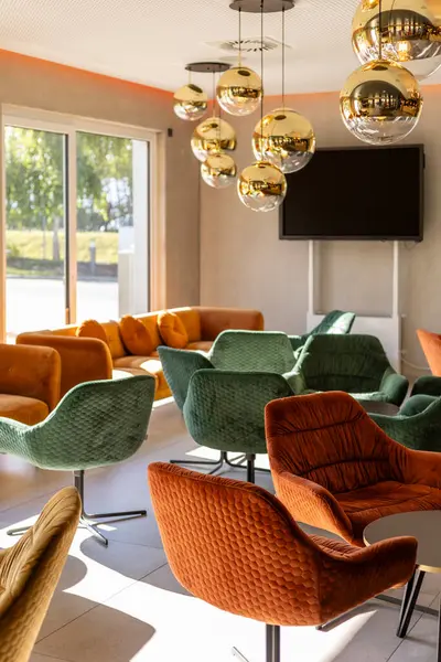 Konforlu koltuklar, yeşil, turuncu ve sarı renkli canlı sandalyelerin yer aldığı çağdaş oturma odasını doldurarak, sosyal toplantılar ve rahatlama için hoş bir atmosfer yaratmaktadır..