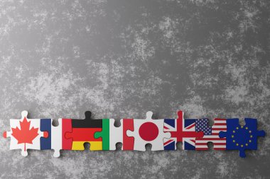 Bulmaca parçaları Kanada, Almanya, İtalya, Japonya, Birleşik Krallık, ABD ve Avrupa Birliği 'nin bayraklarını, uluslar arasındaki birliği simgeleyen dokulu gri bir zemine karşı sergiliyor. Boşluğu kopyala