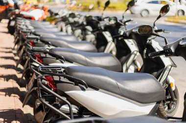 Scooter 'lar hareketli bir şehirde kaldırıma dizilmiş, arabalar geçerken gün ışığını yakalıyorlar. Sahne, şehir yaşamını ve iki tekerlekli taşıma seçeneklerinin popülaritesini yansıtıyor.